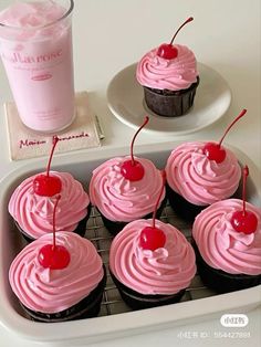 cupcakes with pink frosting and cherries in a tray next to a drink