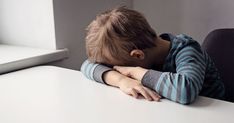 a young boy sitting at a table with his head on his hands and eyes closed