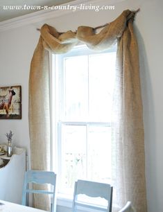 a dining room table with two chairs and a window in the background that has curtains hanging over it