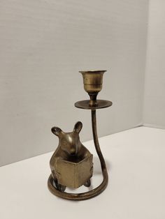 a brass candle holder with a small animal in it's mouth on a white surface