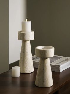 two white candles sitting on top of a wooden table next to a book and candle holder