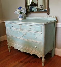 a blue dresser with flowers on top in front of a mirror and wooden flooring