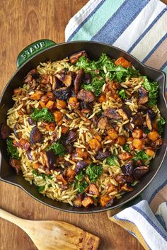 a skillet filled with pasta and vegetables on top of a wooden table next to a cutting board