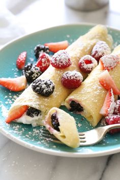 crepes filled with fruit and powdered sugar on a blue plate