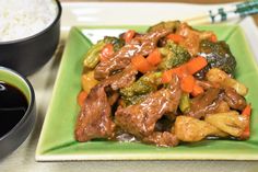 a green plate topped with beef and broccoli next to a bowl of rice