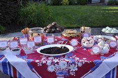 a table covered with lots of food and desserts on top of a red, white and blue table cloth