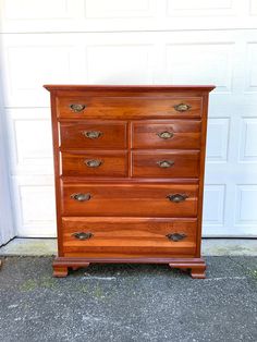 a wooden dresser sitting in front of a garage door with the top drawer open and bottom drawer closed