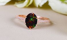 a black opal and diamond ring sitting on top of a white table next to flowers