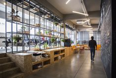 a man walking down the middle of a room with lots of plants on shelves and tables