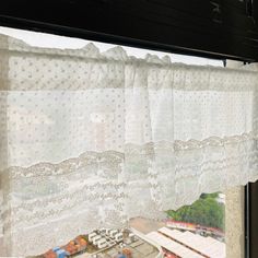 the window is covered with white lace and has a city in the distance behind it