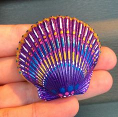 a hand holding a small purple and yellow fan shaped object in it's palm