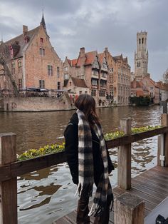 a woman is standing on a dock looking at the water and buildings in the background