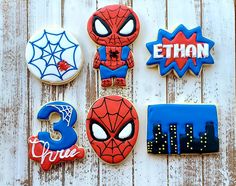 decorated cookies are arranged on a white wooden surface with spiderman, batman, and more