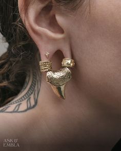 a close up of a person's ear with tattoos on her neck and behind them is a pair of gold earrings