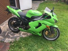 a green motorcycle parked on top of a lush green field next to a building and stone walkway