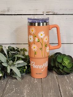 an orange travel mug with white daisies on it and the words powerful written in cursive writing