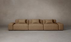 a brown couch sitting on top of a white floor next to a gray wall with lots of pillows