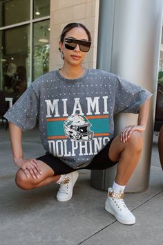 a woman sitting on top of a pole next to a lamp post wearing a miami dolphins t - shirt