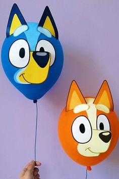 two balloons shaped like cartoon characters are being held by someone's hand on a purple background