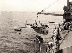 an old black and white photo of people standing on the deck of a ship looking at a plane in the water