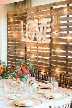 the table is set with plates and glasses for dinner guests to eat in front of the love sign on the wall