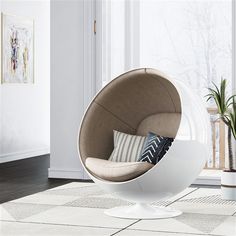 a white egg chair sitting on top of a wooden floor next to a potted plant