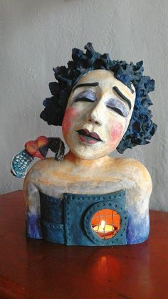 a ceramic sculpture of a woman sitting on a table with a candle in her lap