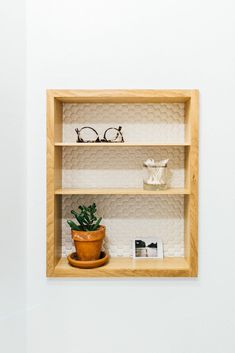 a wooden shelf with glasses on top of it and a potted plant in the middle