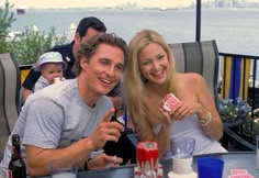 a man and woman sitting at a table with drinks in front of them, posing for the camera