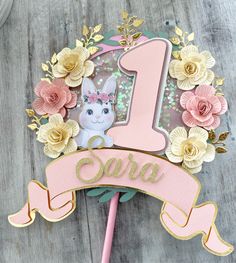 a cake topper with a pink number one on it and flowers in the background