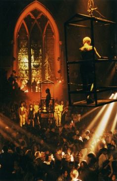 people are standing in front of a stage with lights on it and one person is performing