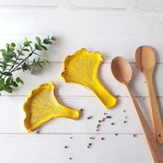 two yellow serving dishes with spoons next to each other on a white wooden surface