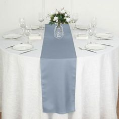 the table is set with white and blue linens, silverware, and flowers