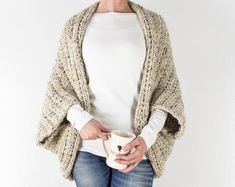 a woman holding a coffee cup and wearing a knitted cardigan over her shoulder