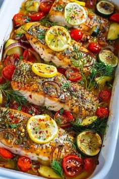 fish with lemons, tomatoes, and herbs in a white casserole dish