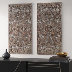 two large metal wall art pieces hanging on a wall next to a black cabinet with a gold bowl