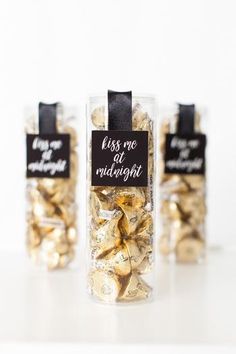 three glass jars filled with gold and black candies that say kiss me at midnight