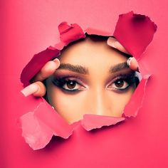 a woman's face peeking through torn pink paper