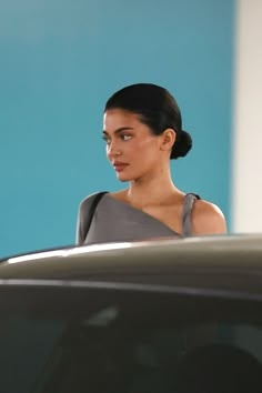 a woman is standing in front of a car and looking off into the distance with her eyes closed