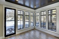 an empty room with large windows and wood floors in the middle of it, looking out onto a snowy yard