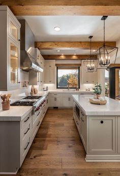 a large kitchen with white cabinets and wood beams on the ceiling, along with wooden flooring