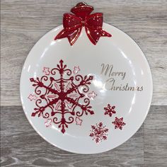 a white plate with a red bow and merry christmas message on it, sitting on a wooden surface