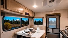 the interior of a travel trailer with windows looking out at trees and water in the distance