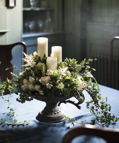 a centerpiece with white flowers and candles on a blue table cloth covered dining room table