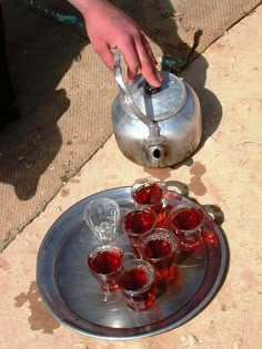 a person is pouring wine into glasses on a silver platter with a tea kettle