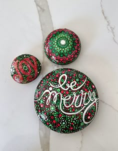 three painted rocks with the words merry written on them, sitting on a marble slab