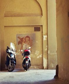 two scooters parked in an alley next to a wall with a painting on it