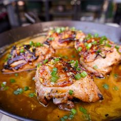 some chicken is cooking in a pan with onions and scallions on the side