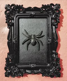 a black framed spider on a pink wall with an ornate border around the frame and it's head