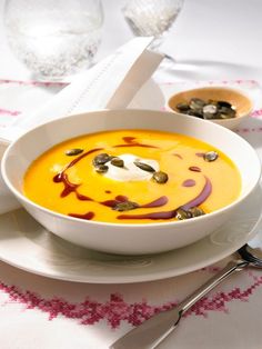 a bowl of soup on a plate with spoons and utensils next to it